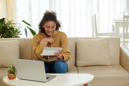 Young adult women opening up mail while sitting on a couch.